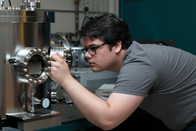 Summer Scholar Grant Smith looks into a sputter deposition chamber, where he makes ultrathin films — from 2 to 10 nanometers thick — of magnetic materials suitable for spin-based electronics such as those used in computer memory systems.