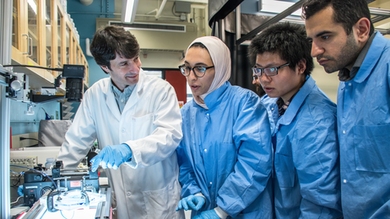Associate Professor Ruben Juanes (left) and students (l-r) Lubna Barghouty, Yunteng Cao, and Ehsan Haghighat discuss the impact of wettability on the patterns of fluid invasion into a porous microfluidic chip, illuminated from below and recorded with a high-speed camera from above. 