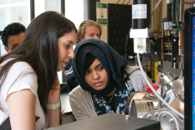 Summer Scholar Abigail Nason (left) and graduate student Takian Fakhrul peer into a pulsed laser deposition chamber for creating thin films that combine magnetic properties and infrared light transparency to serve in waveguides and isolators for integrated photonic chips. 
