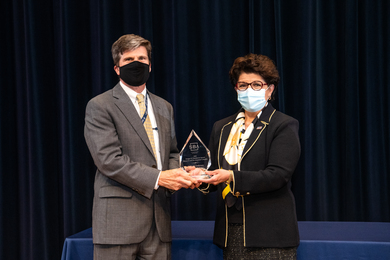 Photo of Jovita Carranza and Scott Anderson, both wearing face masks, holding a glass award.