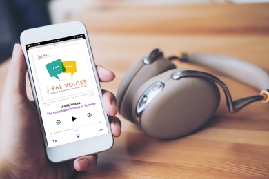 Photo of a hand holding a smartphone with headphones in the background