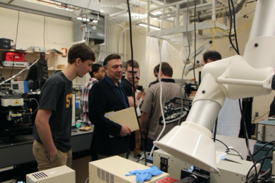 Photo of half a dozen individuals visiting a lab space with machine equipment