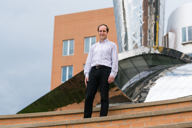 Photo of Antonio Torralba standing at the top of some steps with parts of the MIT Stata Building in the background