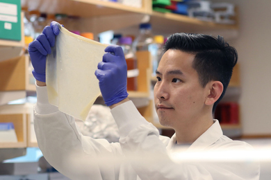 Photo of a man in a white lab coat and blue gloves looking at an opaque white square material