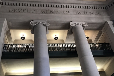 Photo of columns and balconies in MIT Lobby 7 with the etched words "development of science" running around the ceiling