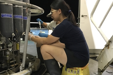 Photo of Tianyi Huang, seated and in profile, drawing seawater samples from an ocean CTD rosette.