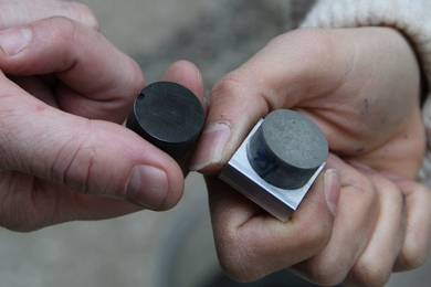 Close-up photo of two people's hands holding cement sample disks.