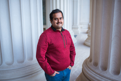 Photo of Arunkumar Seshadri posing amid columns in a red fleece jacket with his hands in his pockets