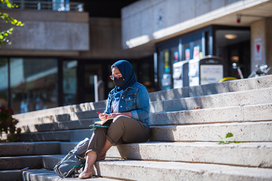 Photo of a student writing in her notebook while sitting on the steps of MIT's student center