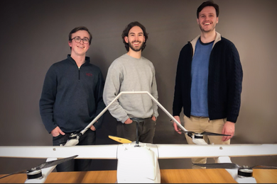 photo of three young men, casually dressed, smiling and standing behind a table with a drone in the foreground