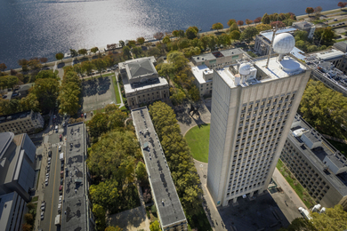 Aerial photo showing a tall MIT building with radar domes on top and a river in background.