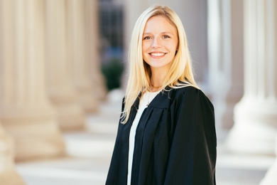 Photo of Grace Moore in a graduation gown on the MIT steps with columns in the background