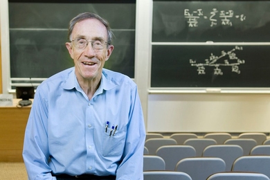 Photo of William Dalzell, smiling and seated before a chalkboard in an empty classroom