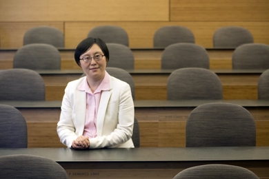 Portrait photo of Siqi Zheng sitting at a long table in an otherwise-empty classroom. 
