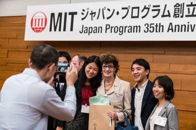 Four people posing for a photographer, with two others in the background