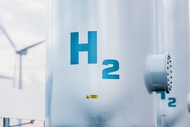 Conceptual illustration of pipes with H2 written on them and windmills and solar panels in the background.