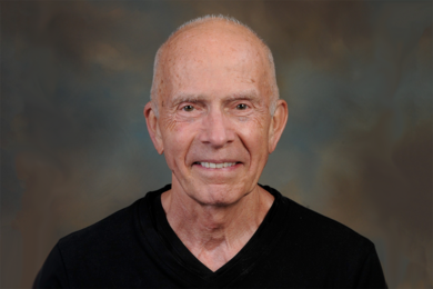 Headshot of Paul Schimmel, an older man with very short white hair smiling in front of a gray background