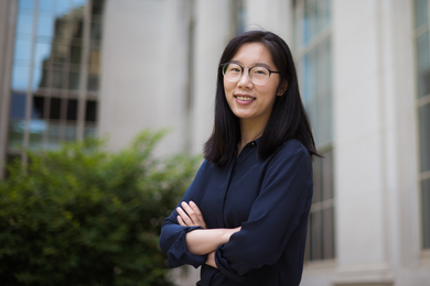 Photo of Limiao Zhang, standing next to the outside of an MIT building with her arms crossed