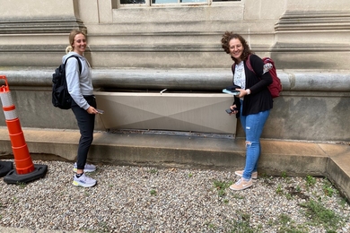Photo of two women taking measurements outside of building vent