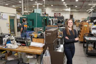 Portrait of Caitlin Braun posing in a large lab space with many tables and pieces of technical equipment