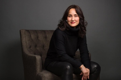 Portrait photo of Cynthia Breazeal, seated, wearing black clothes against a dark background