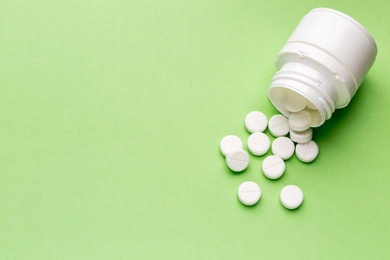 On a light green background a white bottle of pills has tipped over and several small white pills have spilled out.