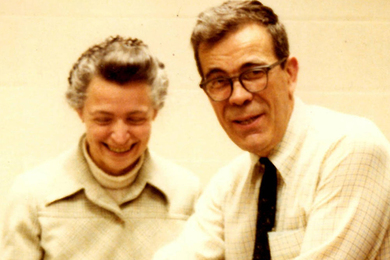 Gene Dresselhaus (right) and Mildred Dresselhaus, both smiling, in front of a white wall. Millie is looking down while Gene looks at the camera.