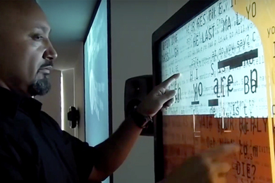 Video-captured image of a man studying data on a wall-mounted screen