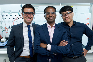 Photo of Karthish Manthiram and two other men, each wearing saftey goggles, posing in front of a lab bench