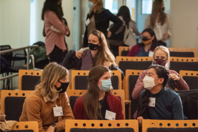 Photo of a group of women sitting in the audience of the research summit, all wearing face masks.
