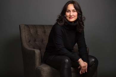 Portrait photo of Cynthia Breazeal, seated, wearing black clothes against a gray background