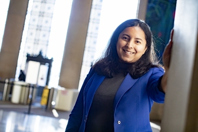 Photo of Kuheli Dutt standing in MIT's Lobby 7, with floor-to-ceiling glass windows behind her