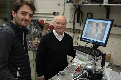 Photo of two smiling men standing at a lab bench covered with electronic equipment