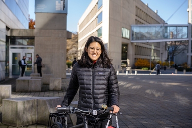 Photo of Laura Rosado wearing a black winter coat and standing with a bicycle