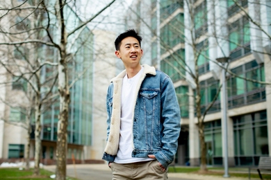 Photo of Daniel Zhang in an unbuttoned, fleece-lined denim jacket, standing with his hands in his pants pockets and looking to one side