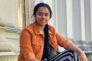 Photo of Akila Saravanan sitting on steps with stone columns behind her