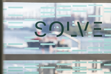 Photo of the MIT Solve logo on a window decal with Boston view in the background 