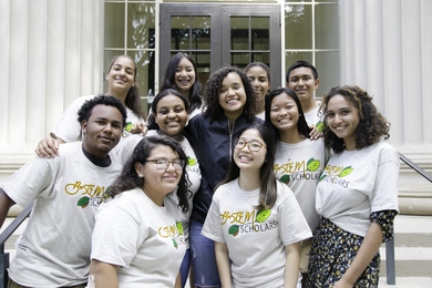 11 smiling people gather for a group photo on steps of the MIT campus