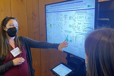 Photo of Adrianna San Roman describing her research in front of electronic poster monitor.