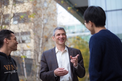 Photo of Jeff Grossman with two graduate students, standing outside with MIT buildings in the background