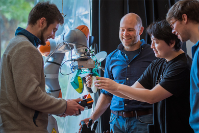 Photo of Professor Russ Tedrake examining a robotic arm with students