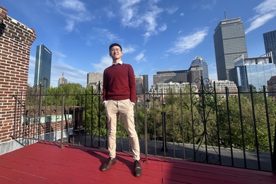 Photo of Chih-Wei Joshua Liu standing on a rooftop with the Boston skyline in background.