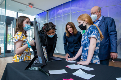 Photo of three children sharing their project on a computer screen with Karyn Polito and Jeffrey Leiden