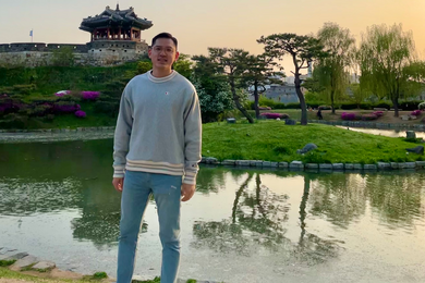 Jung Jae Kwon poes for a photo in front of a pond, trees, and an Asian-style gazebo