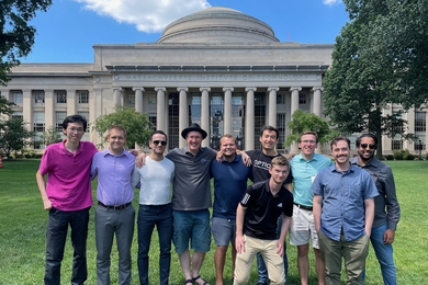 Group of 10 people posing on the grass in front of the MIT Dome