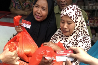 Photo of two women presenting ID cards to receive large orange bags of rice