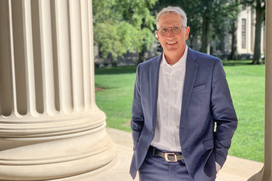 Joe Higgins stands next to a large stone column in front of the grass on MIT's Killian Court