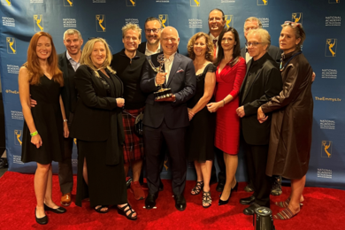 The 12-person “The Hunt for Planet B” team poses on the red carpet. The director smiles and holds the Emmy trophy in the center of the shot. 