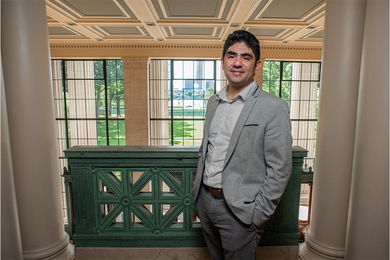 Christopher Mejía Argueta stands on a balcony in MIT's Building 10, looking out onto the grassy Killian Court