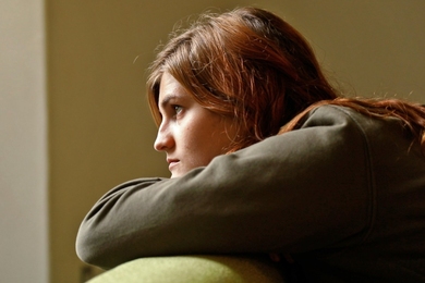 Side profile of Emily Satterfield resting her head in her arms over the side of a chair and gazing into the distance